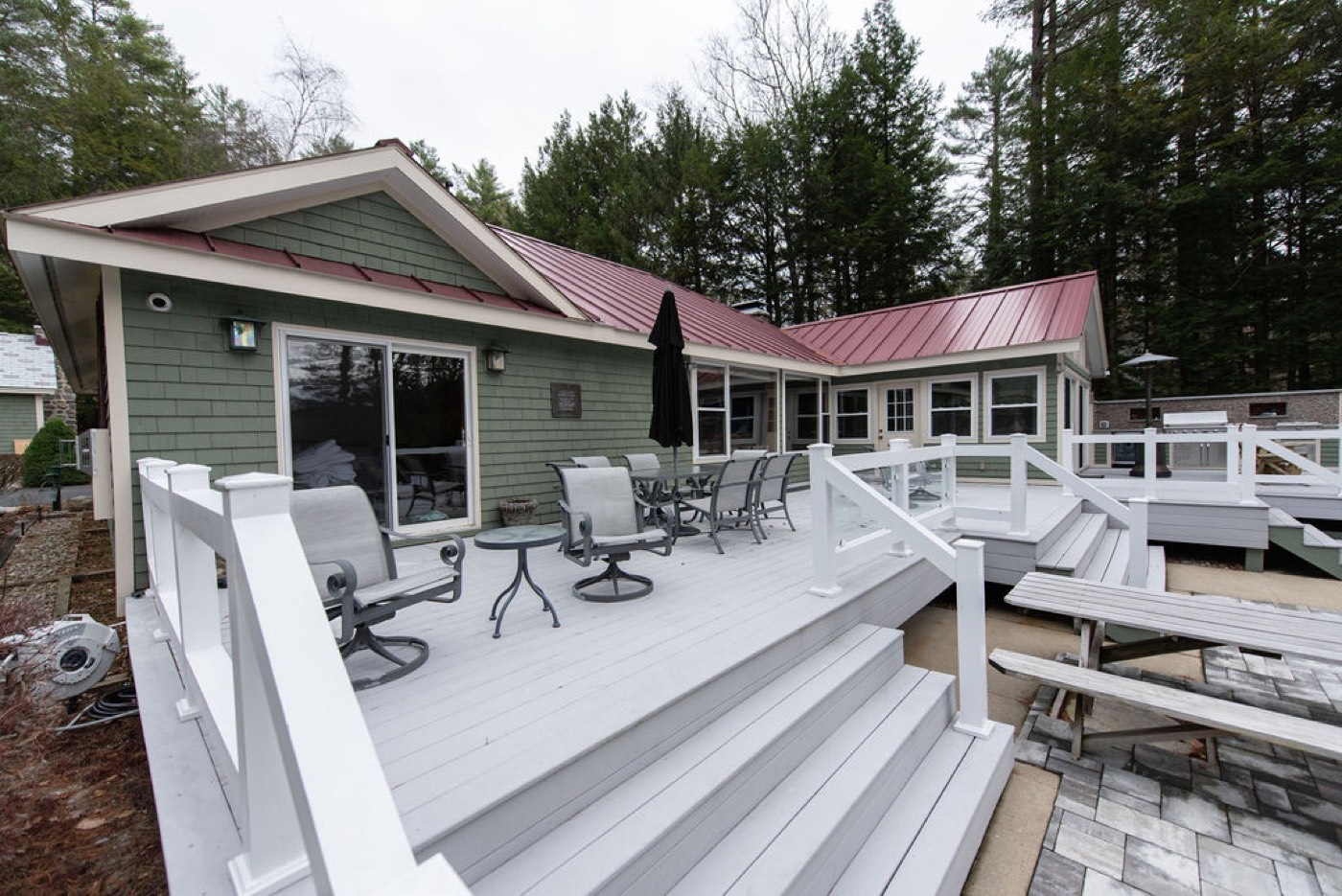 The lakeside deck at Camp Sunnyside with dining seating under the sage-shingle main house and its barn-red metal roof.