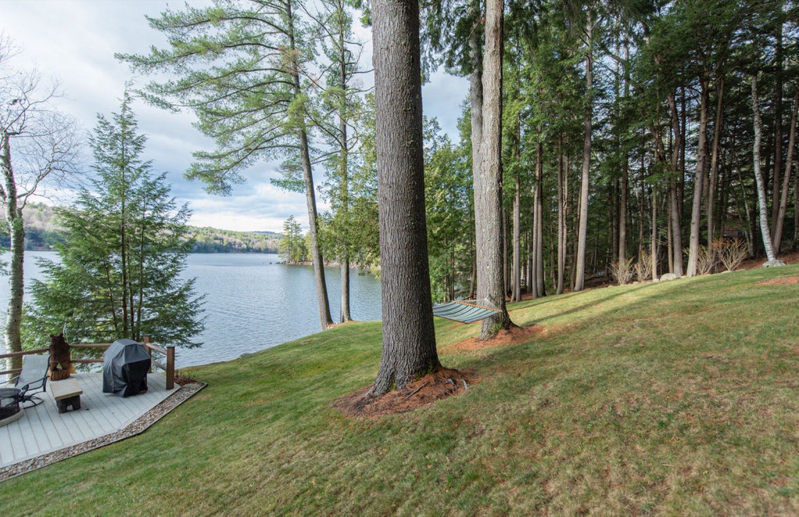 A hammock strung between tall pines above the sloping lawn to the waterfront deck and Friends Lake at Camp Sunnyside.
