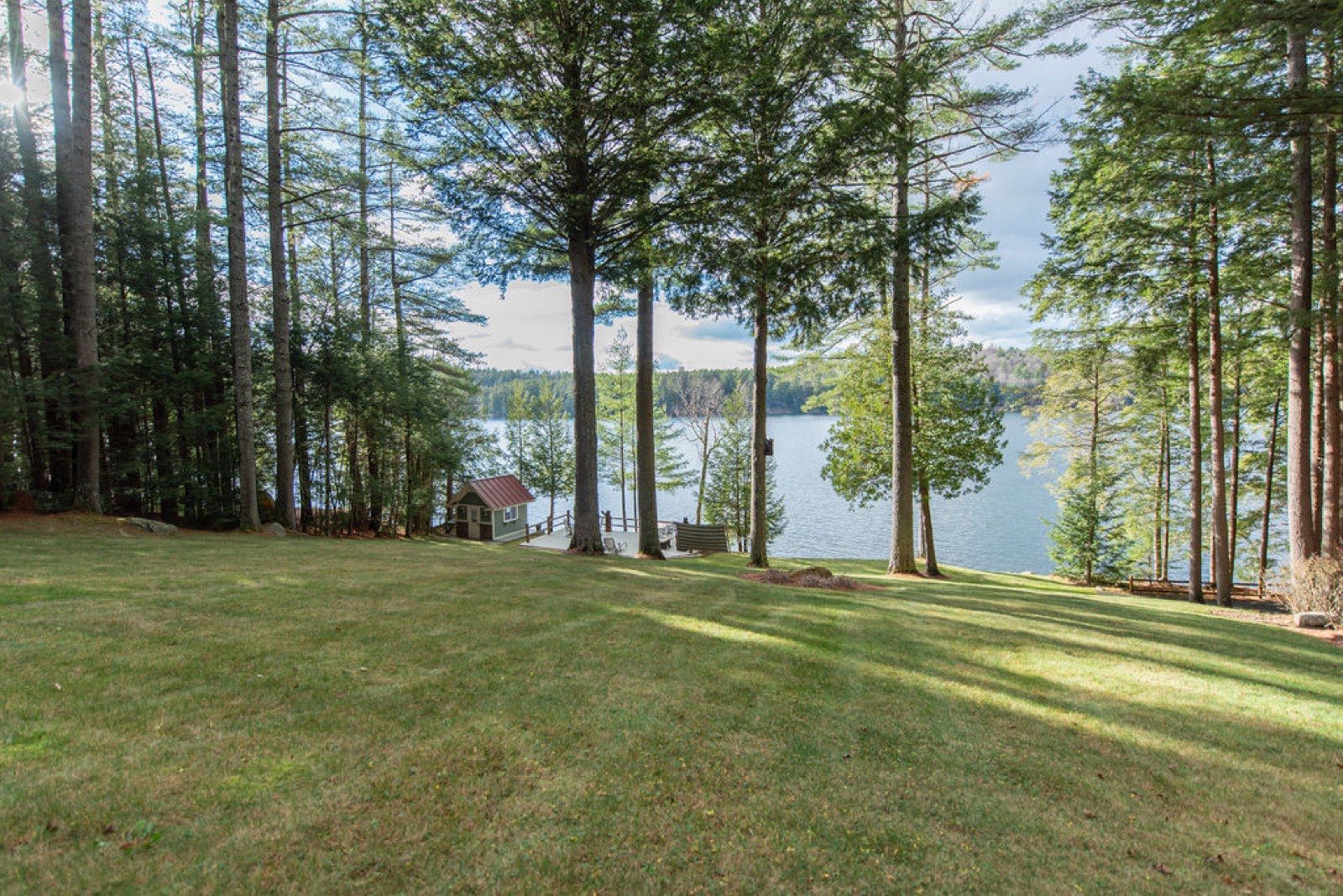 The wide lawn sloping down through tall pines to the dock and boathouse on Friends Lake at Camp Sunnyside.